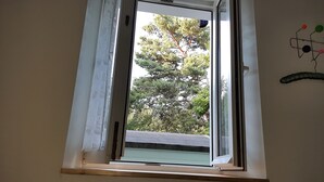 A window with a view of trees and a roof. - La maison verte, a charming and modern two-room apartment (Strasbourg)
