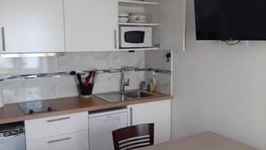 A compact kitchen with white cabinets, a microwave, a sink, and a dining area with a table and chairs. - La maison verte, a charming and modern two-room apartment (Strasbourg)