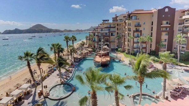 Een resort met een groot zwembad, palmbomen en uitzicht op zee.