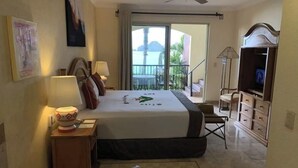 Een hotelkamer met een bed, een badkamer met een wastafel, een televisie en een balkon met uitzicht op zee.