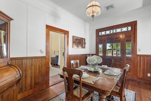 Comedor con una mesa de madera dispuesta para seis personas, rodeada de sillas de madera, una araña y un ventanal con vitrales.