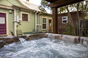 Un jacuzzi en un patio trasero con una terraza de madera, un invernadero y una ventana pequeña.