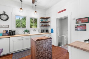 Una cocina moderna con armarios blancos, una zona de café, microondas y un estante decorativo en la pared.