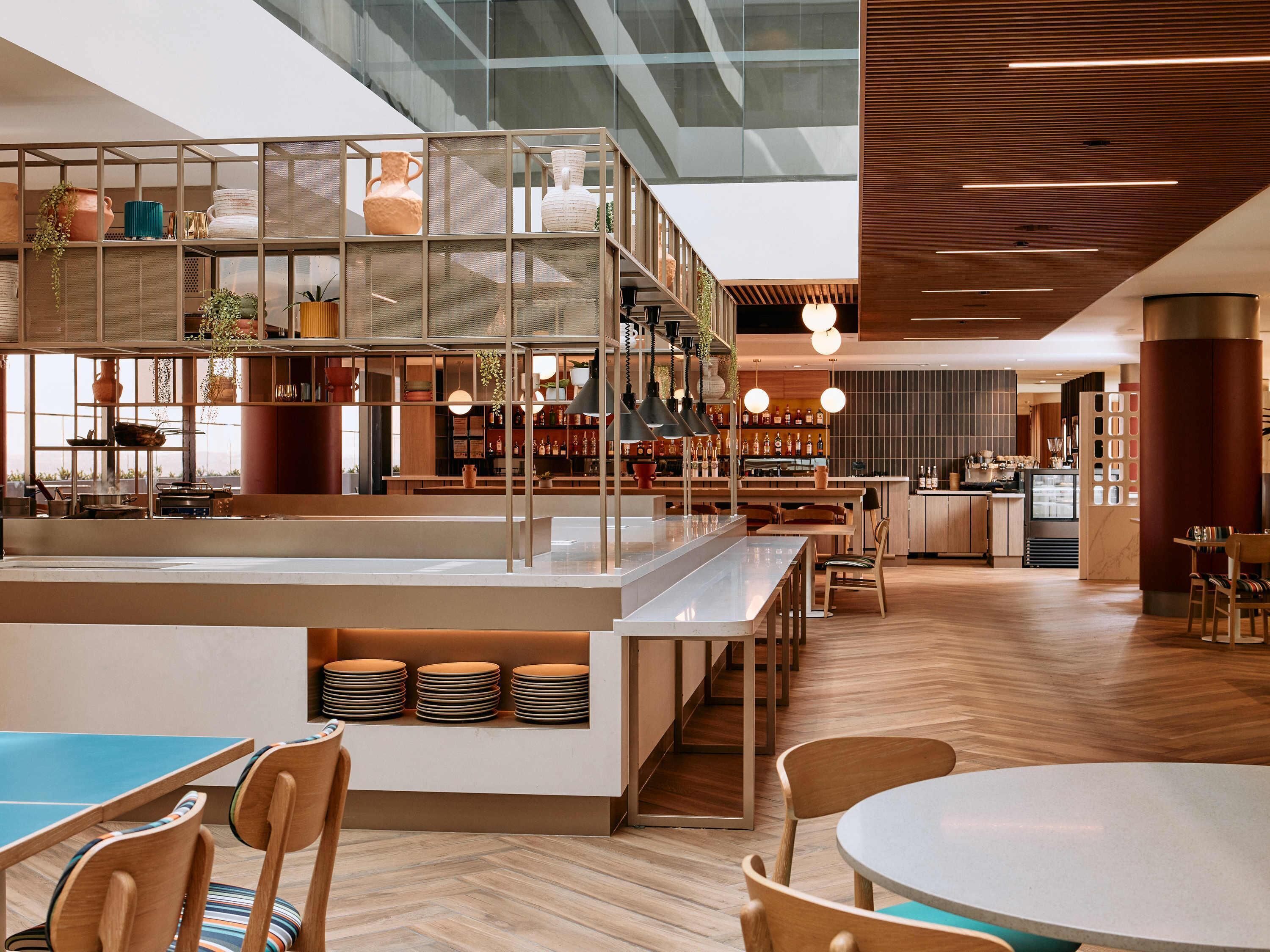 A modern restaurant with a mezzanine level, wooden flooring, and a variety of seating options including tables and chairs.