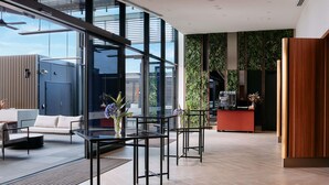 Un moderno vestíbulo de hotel con paredes de vidrio, una recepción y un área de descanso con una cafetera.