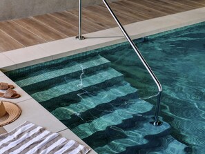 Piscina limpia con escalones de acceso, una baranda metálica y un par de sandalias y un sombrero de paja al borde.