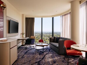Una habitación de hotel moderna con un ventanal grande, un televisor de pantalla plana, un sofá, una mesa de comedor y un escritorio.