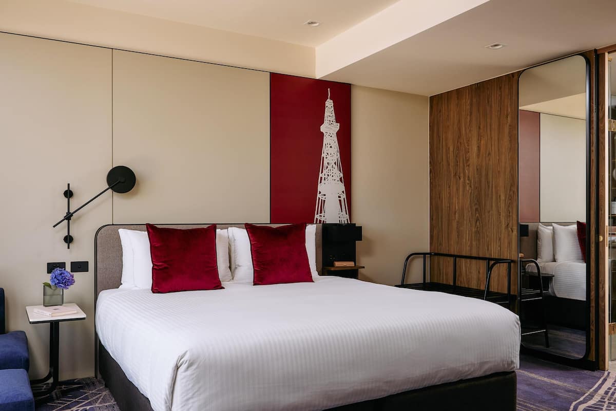 A hotel room with a large bed, a side table, a mirror, and a wall-mounted artwork.