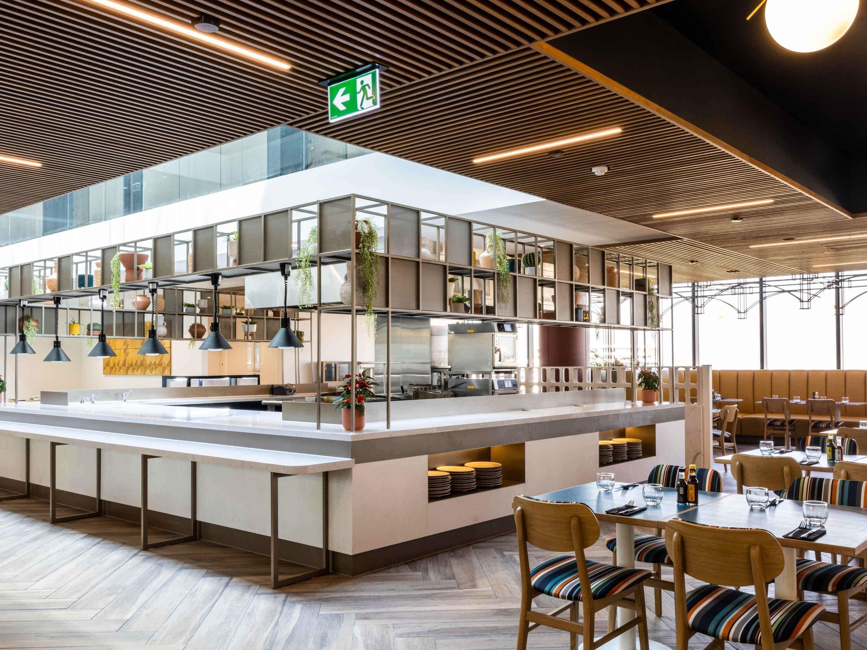 A modern restaurant with a central island, seating area, and a ceiling with linear lighting.