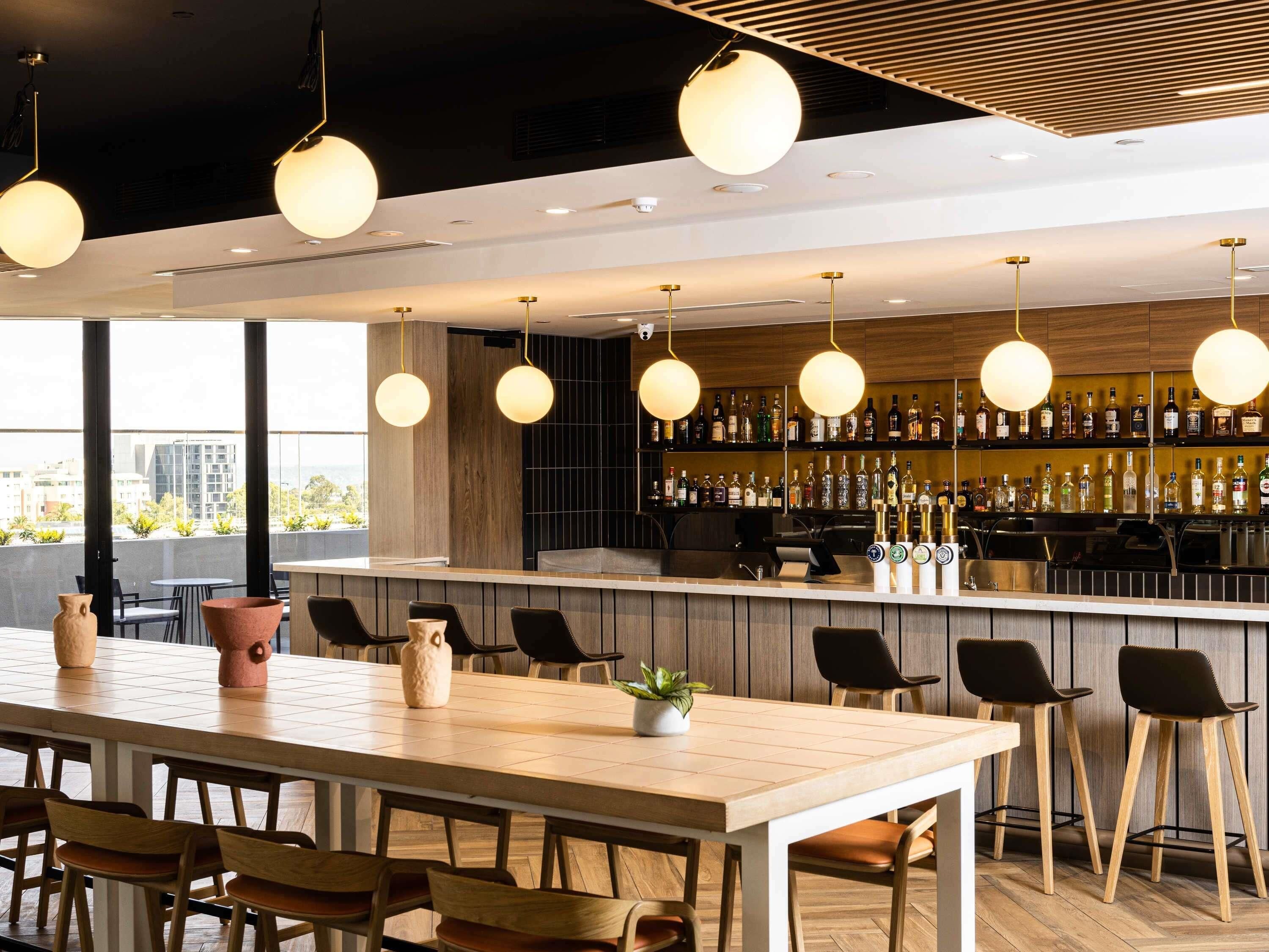 Eine moderne Bar mit einer langen Theke, mehreren hängenden Lampen und einer Auswahl an Flaschen in Regalen.