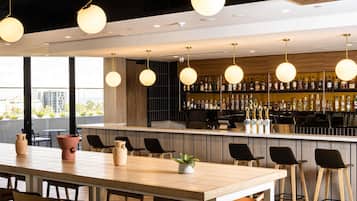 Eine moderne Bar mit einer langen Theke, mehreren hängenden Lampen und einer Auswahl an Flaschen in Regalen.