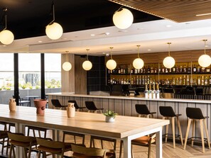A modern bar area with a long counter, multiple hanging lights, and a variety of bottles on shelves. - Mercure Melbourne Doncaster (Doncaster)
