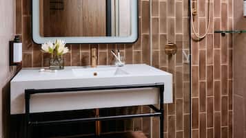 Un baño moderno con un lavamanos blanco, un mueble de madera, cabina de ducha con mampara de vidrio y un espejo con marco de madera.