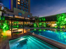 Zona de piscina con sillones de descanso y un espacio de estar techado, rodeada de vegetación y arquitectura moderna.