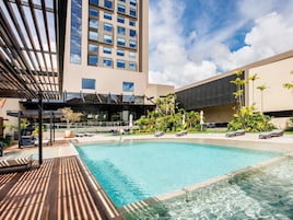 Un hotel moderno con piscina, mobiliario exterior y vistas a un edificio alto.