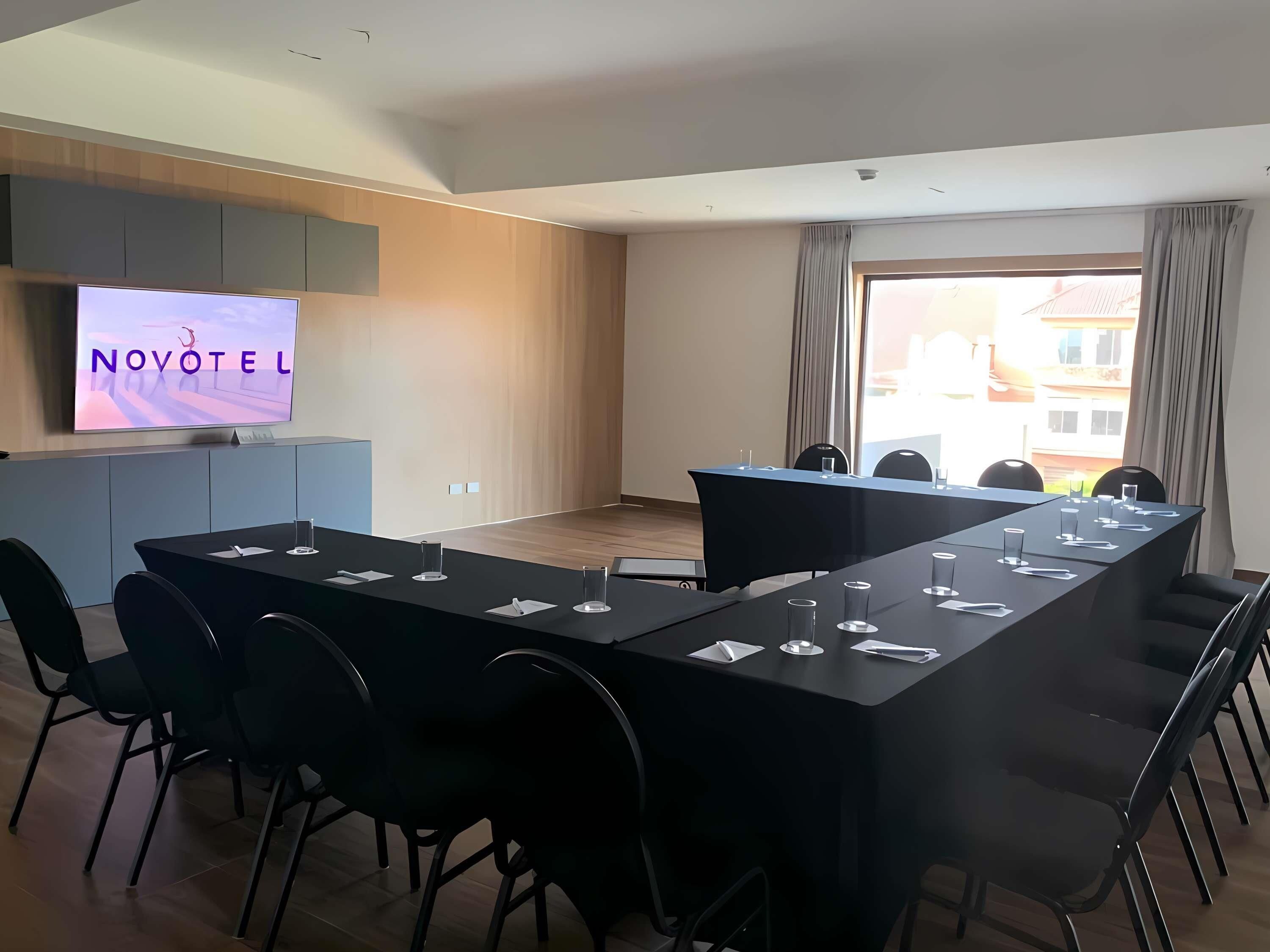 Ein Konferenzraum mit langem Tisch, Stühlen, einem Fernsehbildschirm und einem Fenster mit Vorhängen.