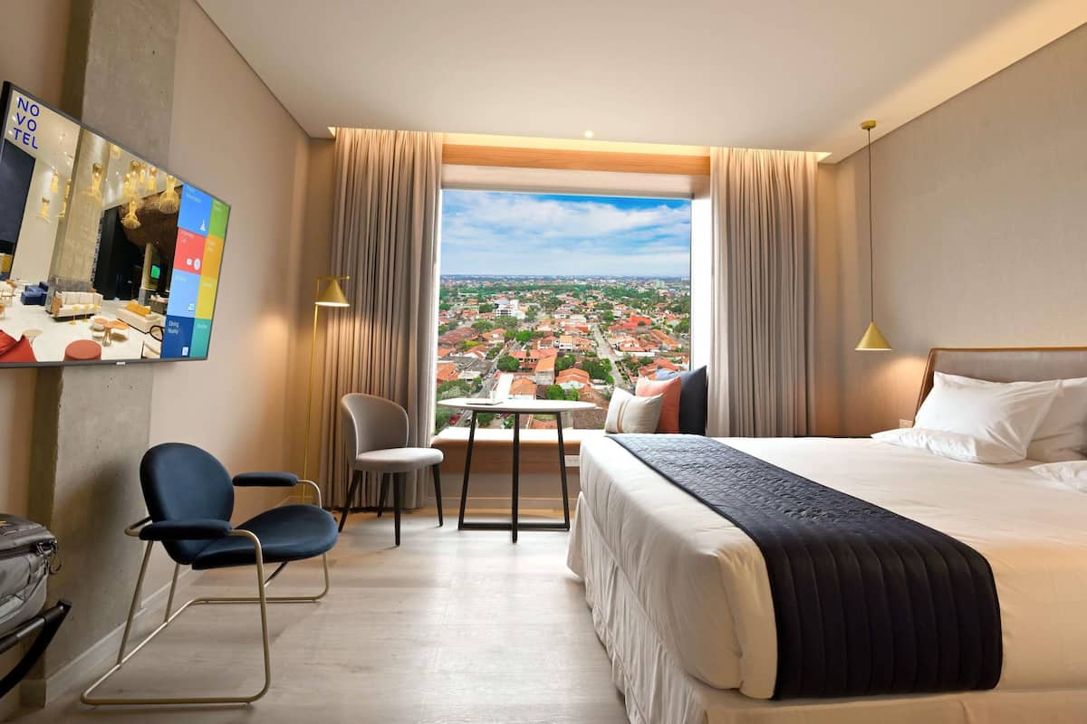 Une chambre d’hôtel avec un grand lit, un bureau, une chaise et une vue sur le paysage urbain.