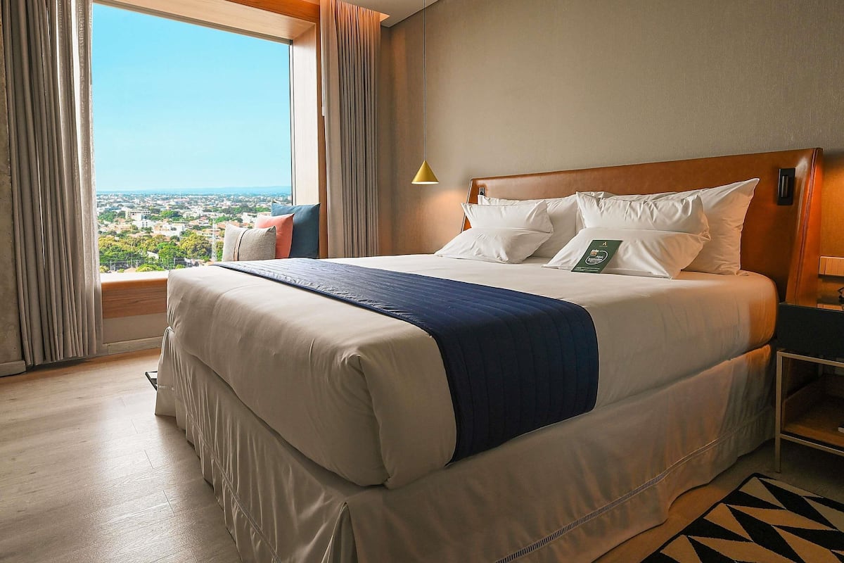 Une chambre d’hôtel avec un grand lit, une vue sur la ville et une table de chevet avec une lampe.
