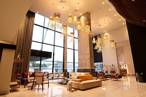 Un hall espacioso con grandes ventanales, candelabros modernos y un área de descanso con sofás y sillones.