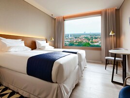 Habitación de hotel con dos camas, una mesita y vista a un paisaje urbano.