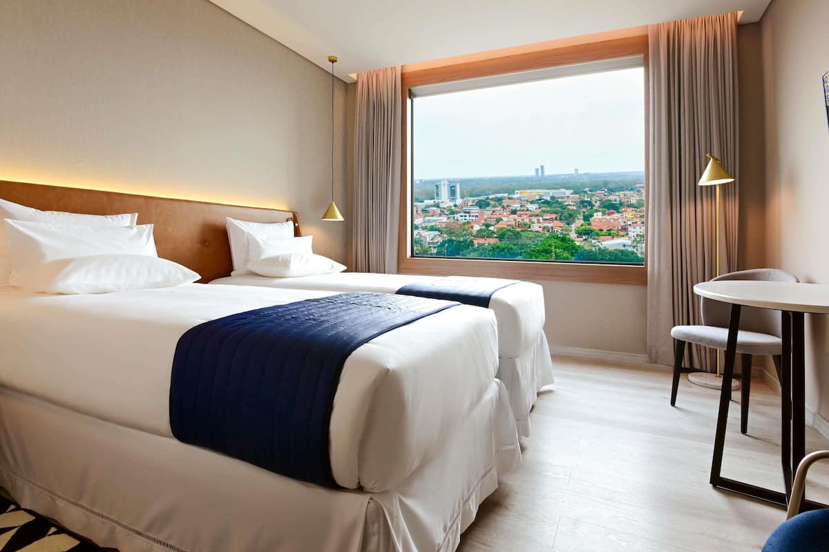 Une chambre d’hôtel avec deux lits, une petite table et une vue sur le paysage urbain.