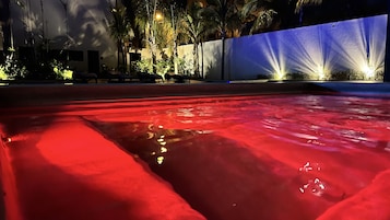 Una piscina con iluminación roja, rodeada de palmeras y un muro blanco.