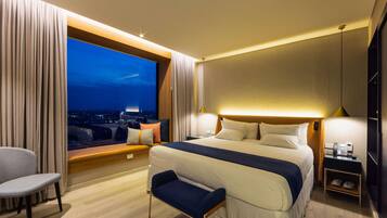 A hotel room with a large bed, a seating area, a view of the city at night, and a phone on the nightstand.