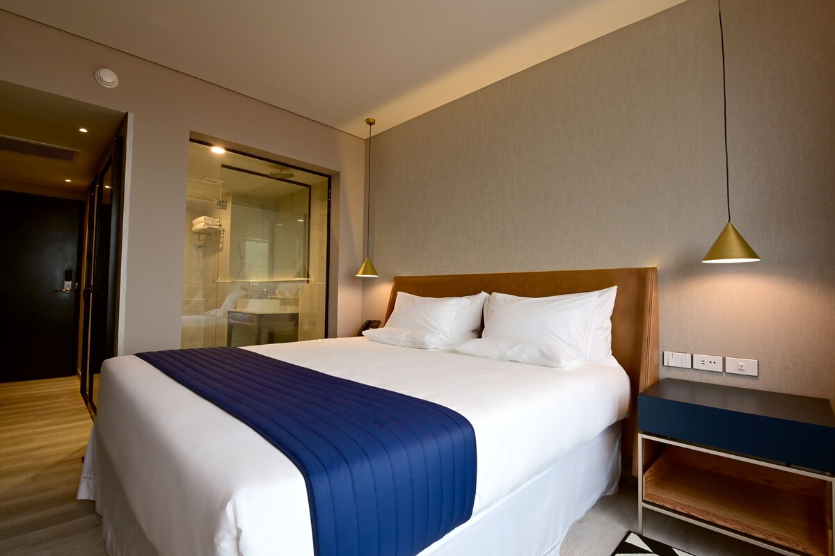 Une chambre d’hôtel avec un grand lit, une table de chevet, un miroir et une porte donnant sur une salle de bain.