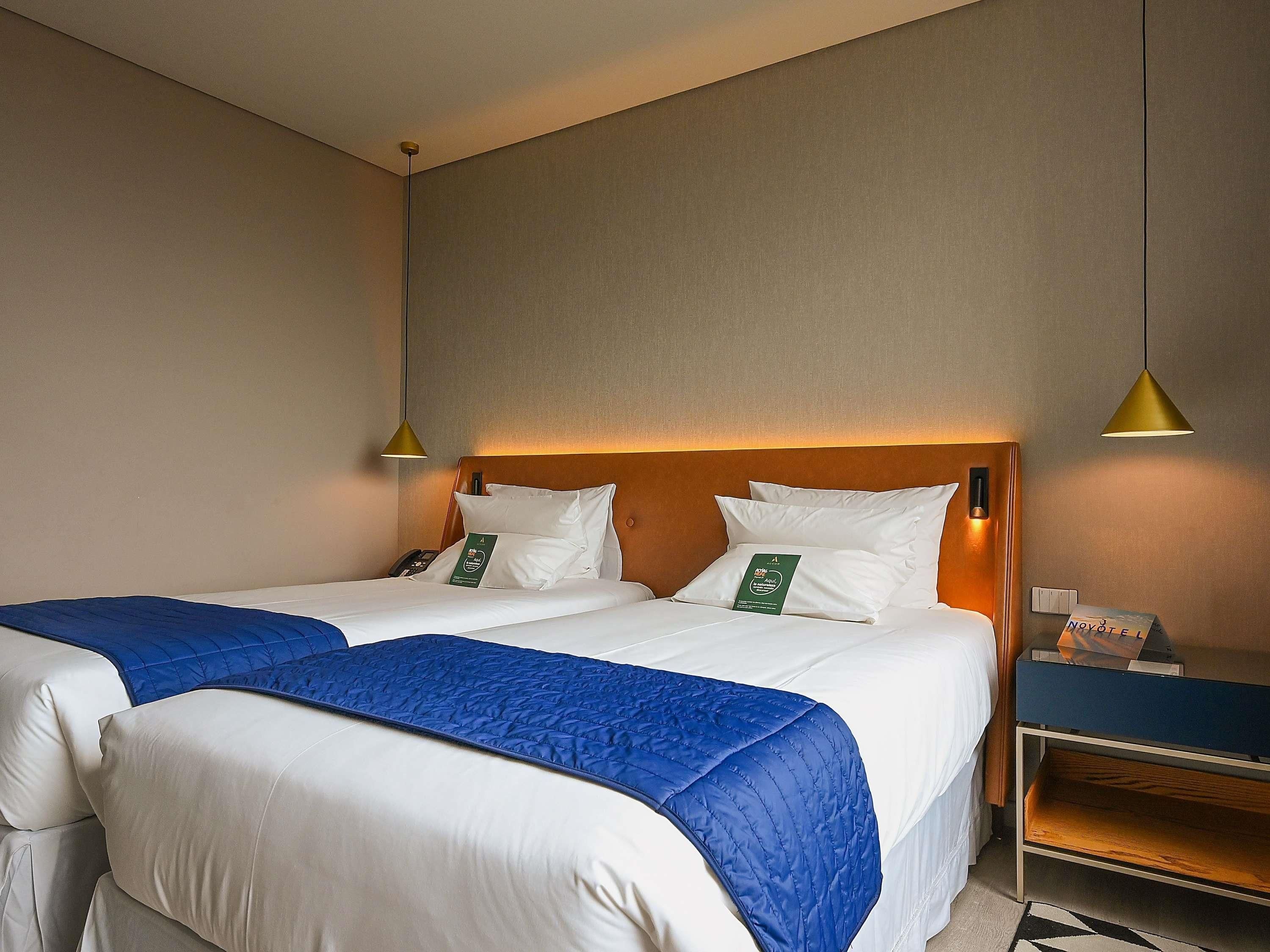 Ein Hotelzimmer mit zwei Betten, einem Holz-Kopfteil, einem Nachttisch mit Lampe und einem kleinen Regal.