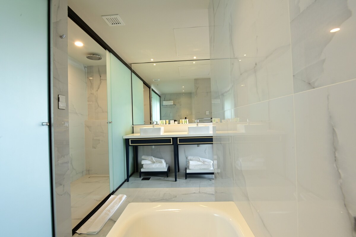 Une salle de bain moderne dotée d’une douche à parois de verre, d’une grande baignoire et d’un meuble-lavabo double avec deux vasques.