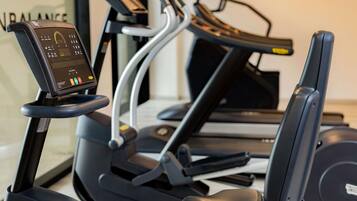 Ein Standfahrrad mit digitalem Display, ein Laufband und ein Rudergerät in einem Fitnessstudio.
