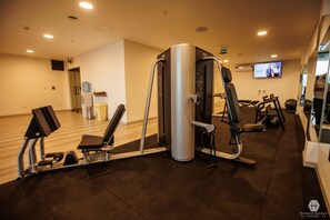Un centre de remise en forme équipé d’appareils de cardio, d’un distributeur d’eau et d’un écran de télévision diffusant une émission.
