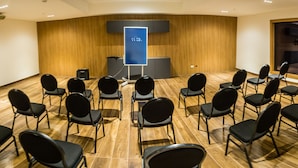 Een vergaderzaal met rijen stoelen gericht op een spreekgestoelte met een digitaal scherm.