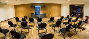 Une salle de conférence avec des rangées de chaises disposées face à un pupitre équipé d’un écran numérique.