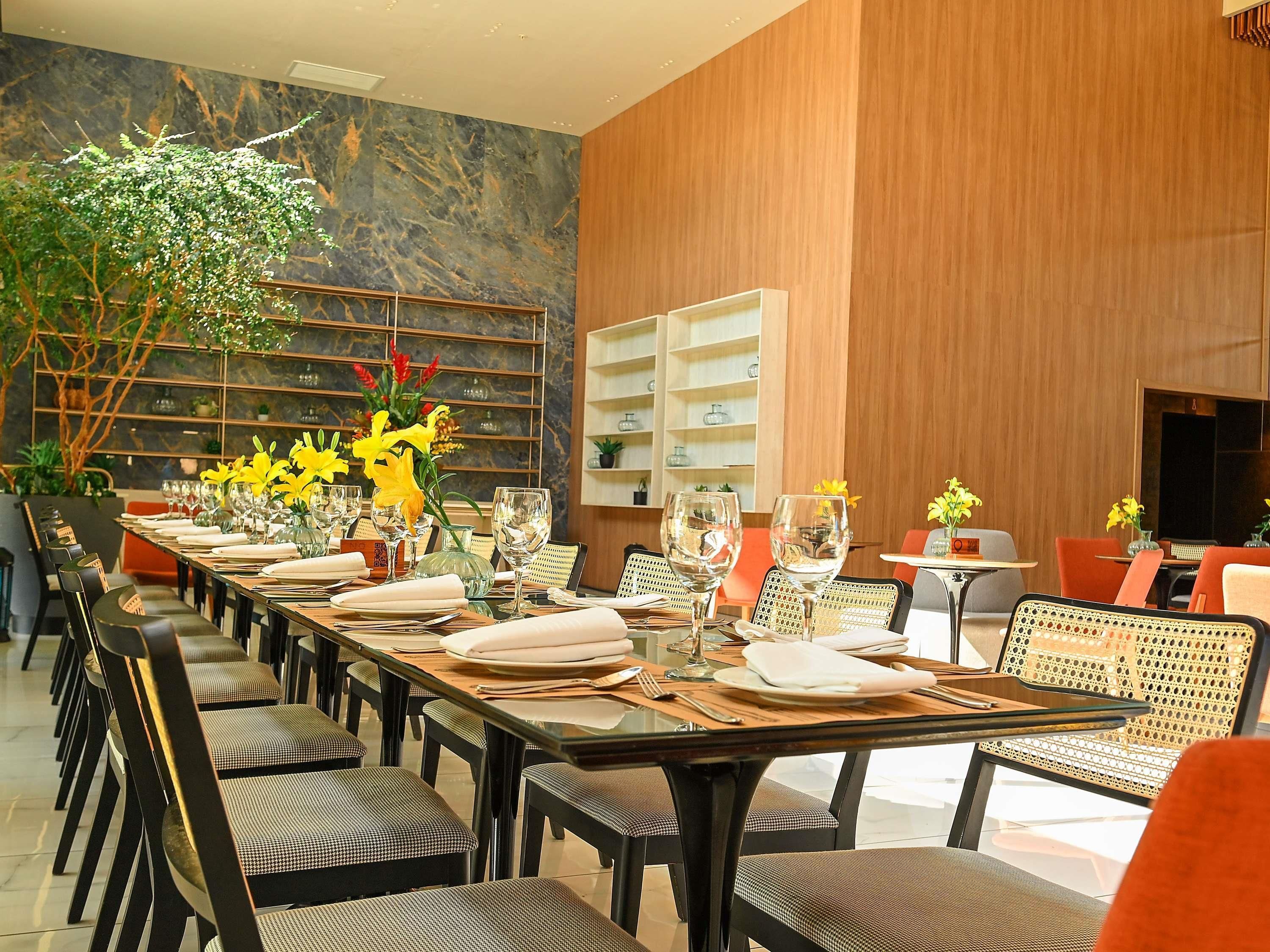 A modern dining area with a long table set for a meal, surrounded by chairs, and a decorative plant with yellow flowers.