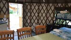 A room with a bunk bed, a table with chairs, a desk, and a window with a view of the outside.