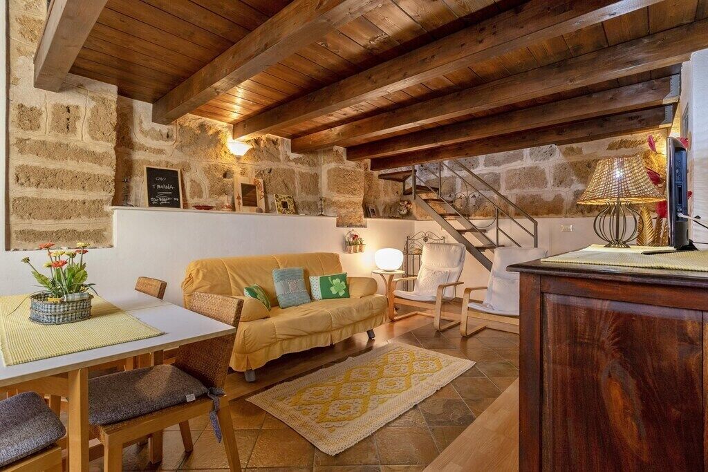 Ein gemütliches Zimmer mit Holzbalkendecke, Steinwänden, einer Couch, einem Tisch und einem Sessel.