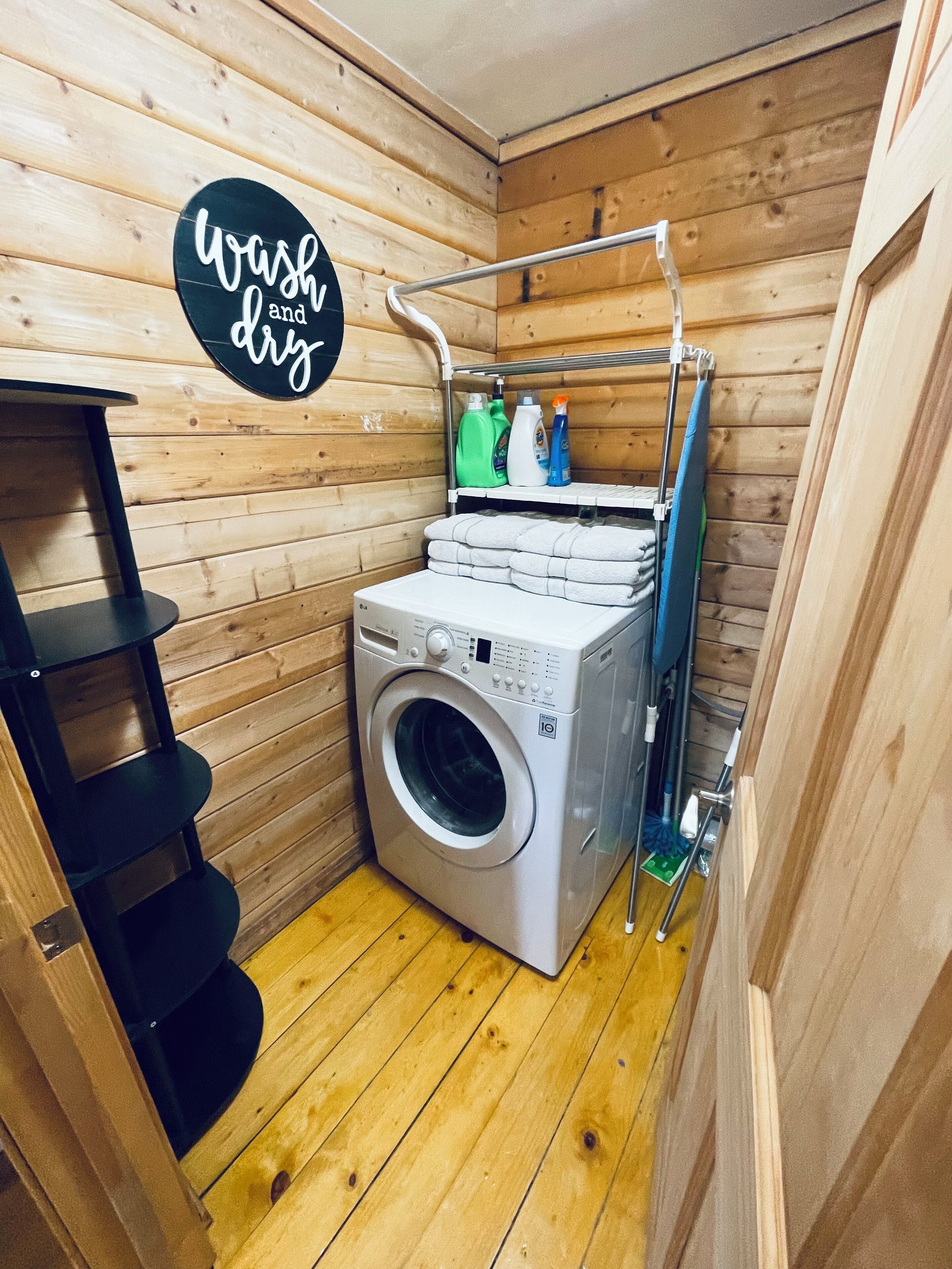 Une petite buanderie équipée d’un lave-linge, d’étagères contenant des produits de nettoyage et d’un panneau indiquant « laver et sécher ».