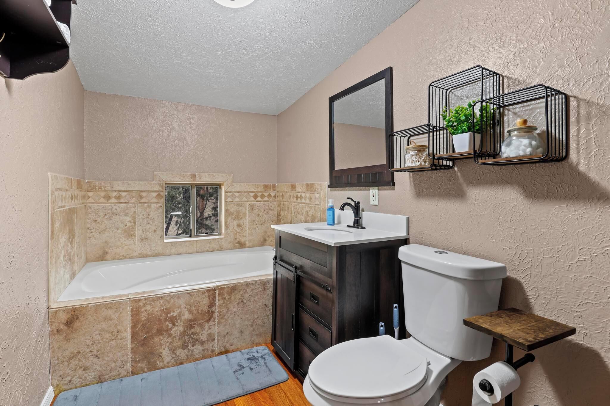 A bathroom with a bathtub, toilet, sink, and a mirror. There are three shelves with plants and jars.