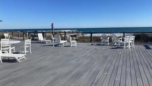 Eine Holzterrasse mit weißen Stühlen und Tischen, mit Blick auf den Ozean.