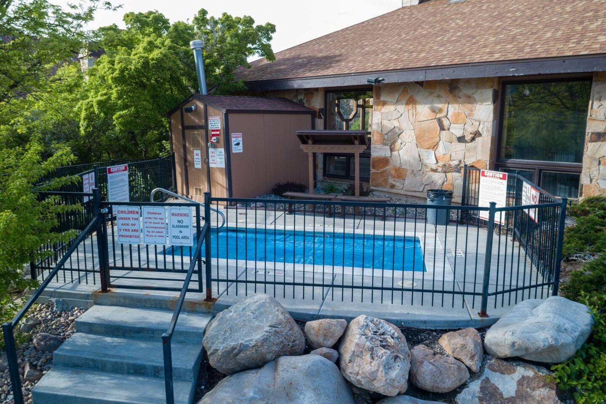 A pool area with a stone building, a covered seating area, and a metal fence.