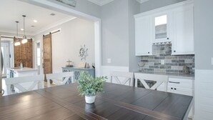 Una cocina moderna con armarios blancos, un salpicadero de ladrillo y una zona de comedor con una mesa y sillas de madera oscura.