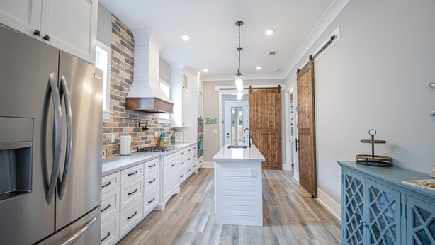 Una cocina moderna con refrigerador de acero inoxidable, armarios blancos, una isla central y una puerta de madera.
