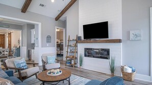 Una sala de estar con chimenea, un televisor montado encima y un comedor al fondo.