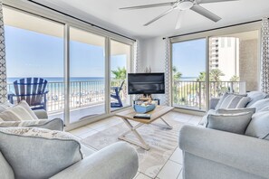 A spacious balcony with a TV, seating area, and a view of the beach.