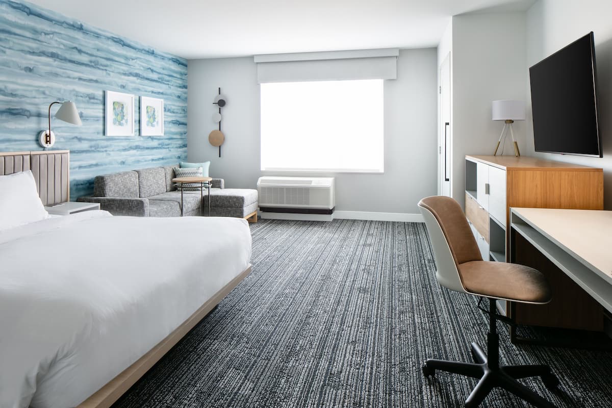 Een hotelkamer met een bed, een bureau, een stoel, een televisie, een raam en een muur met een blauw patroon.