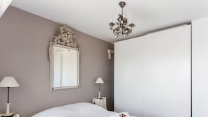A neatly made bed with white linens and rolled towels, a large mirror with an ornate frame, a chandelier, and a white wardrobe. - Le Panoramique Croisette - Welkeys (Cannes)