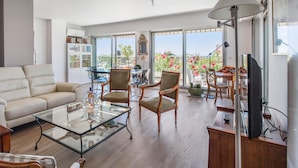 A spacious living room with a glass coffee table, comfortable seating, and a large window offering a view of the outdoors. - Le Panoramique Croisette - Welkeys (Cannes)