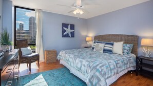 Een slaapkamer met een groot bed, een plafondventilator, uitzicht op de stad en een raam met gordijnen.