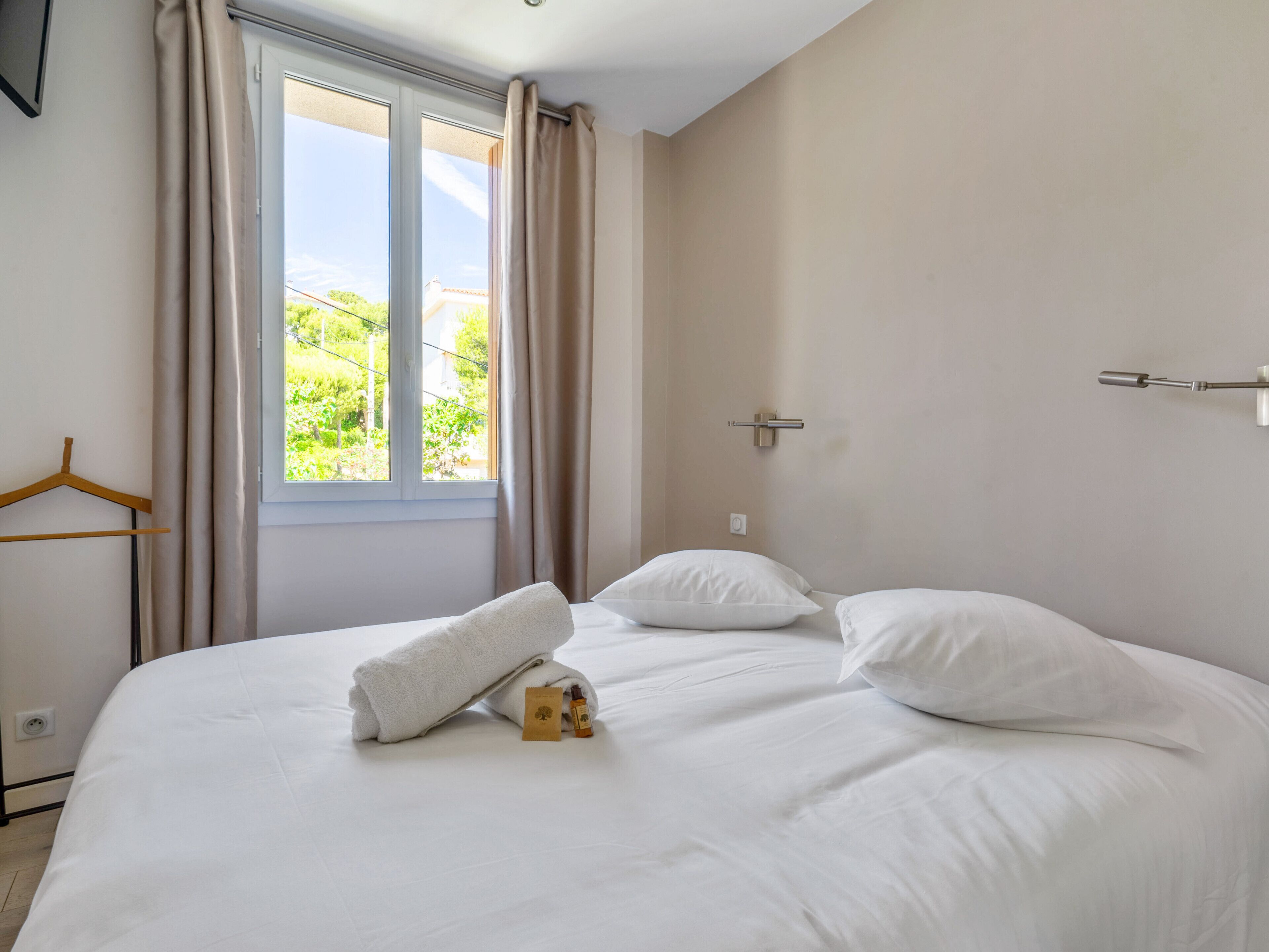 Un lit bien fait, avec des draps blancs, une serviette suspendue et une bouteille de lotion posée sur le lit.